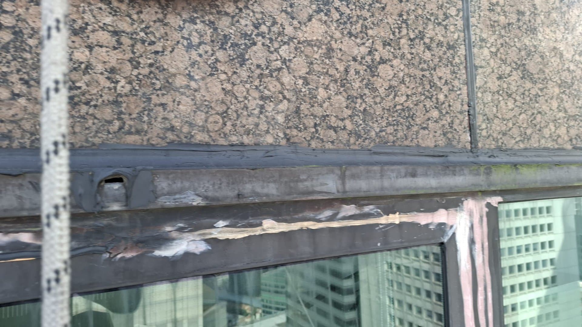 Aged, peeling façade sealant on the joint above a glazing panel of a Singapore high-rise, due for rope-access resealing