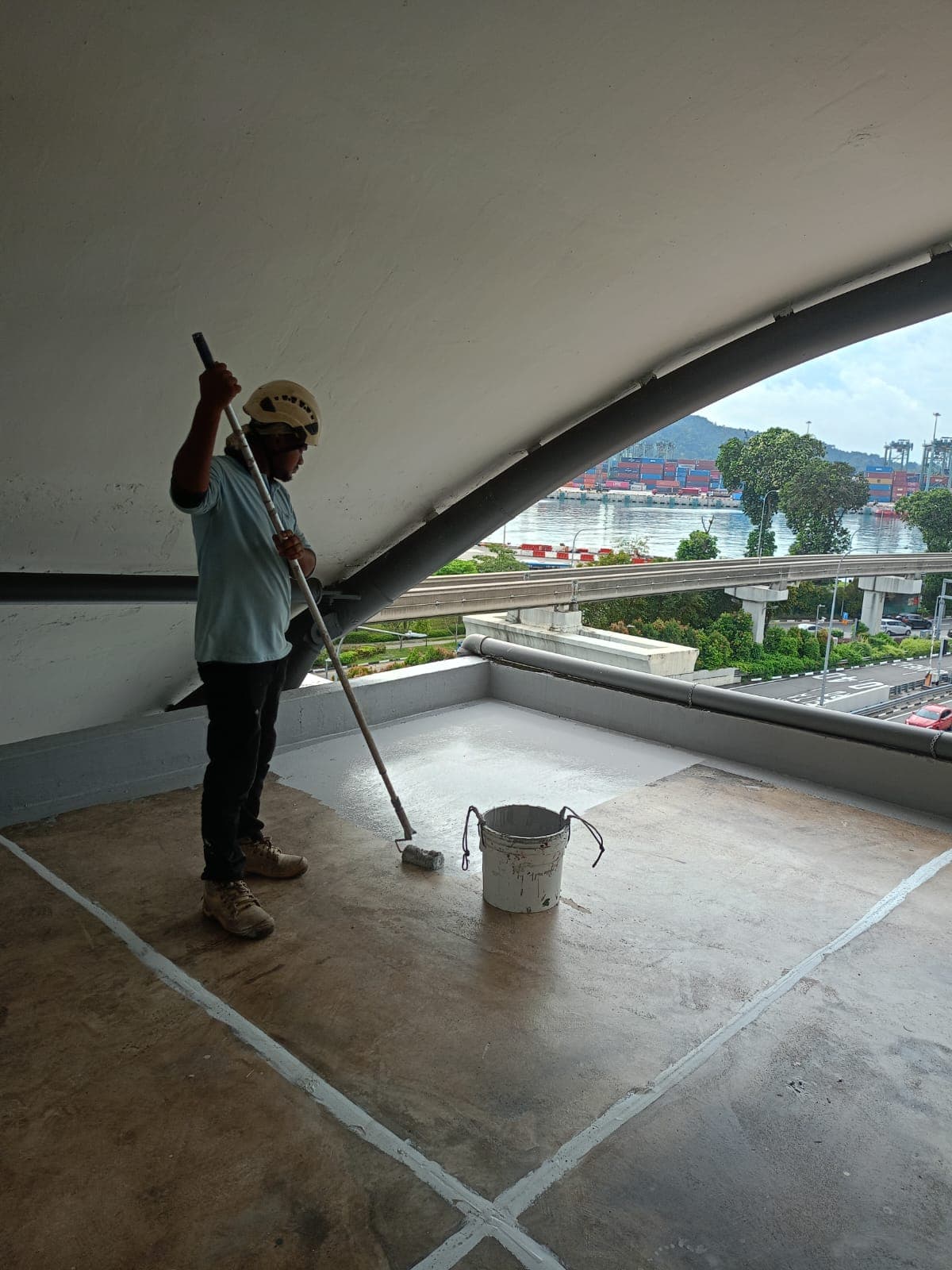Hydroseal technician roller-coating a curved concrete soffit at a Singapore waterfront structure