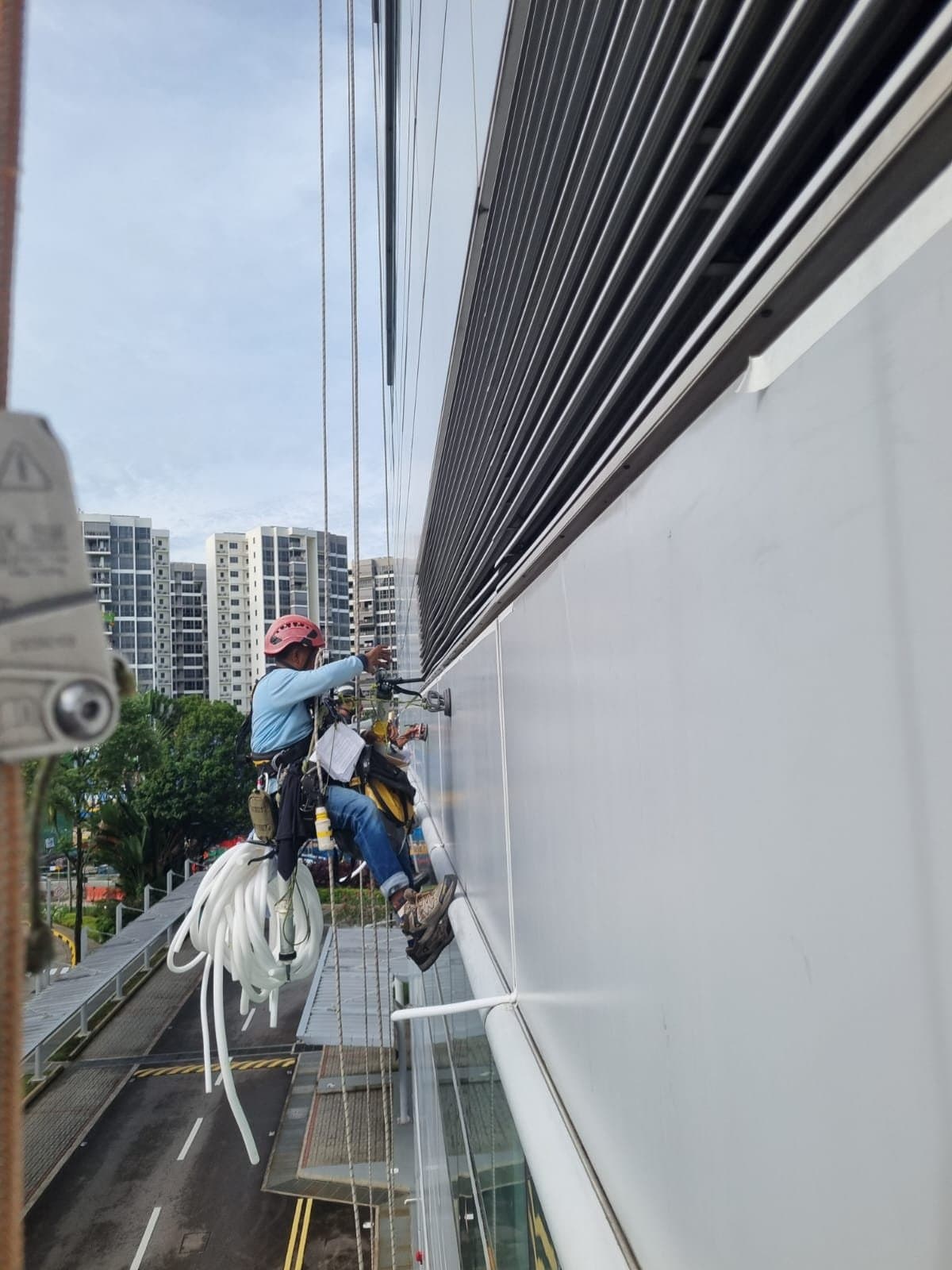 Hydroseal rope-access technicians resealing the external-wall joints of a Singapore condominium, with neighbouring residential blocks behind