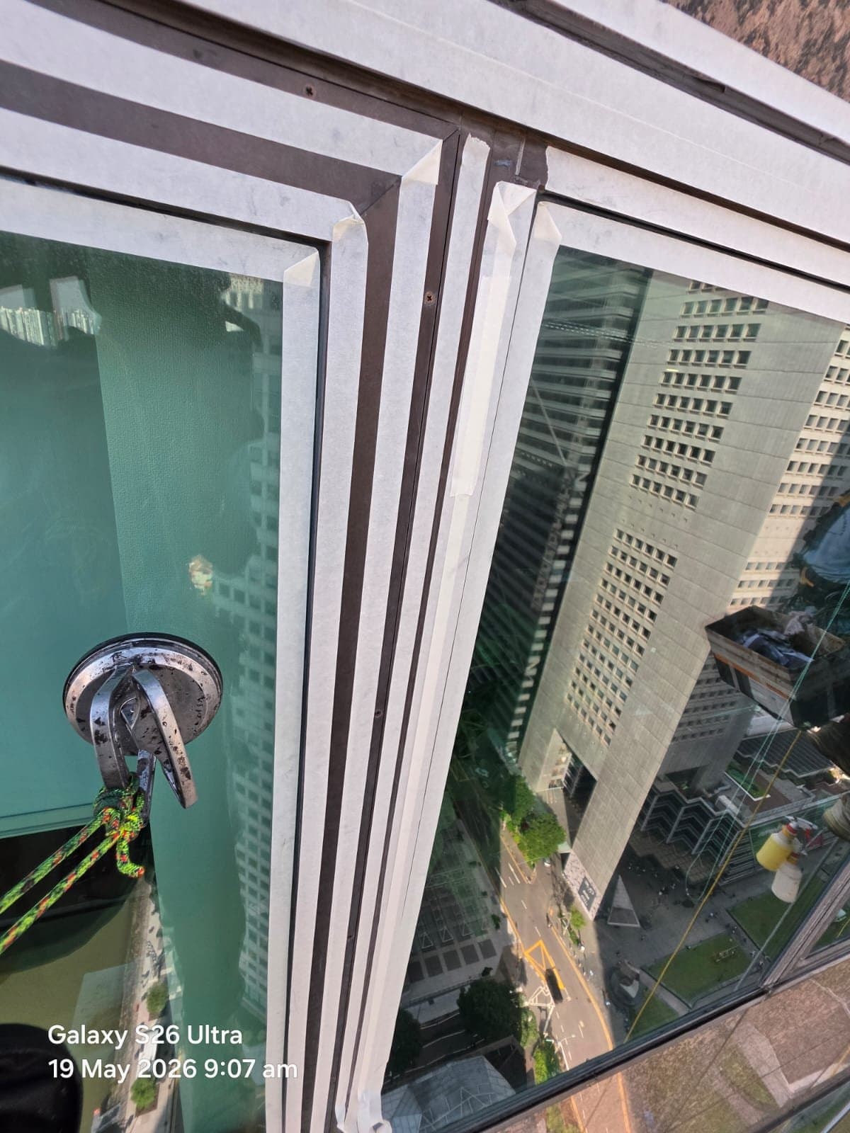 Hydroseal façade sealant preparation with masking tape and a suction anchor on the glazing of a high-rise office tower, the CBD streets far below