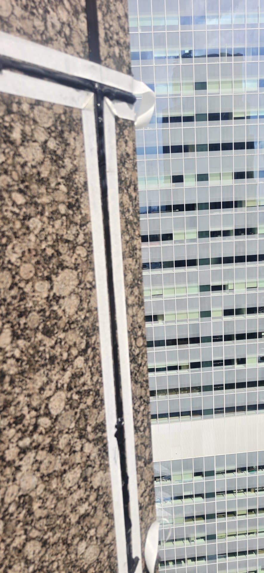 Close-up of a finished Hydroseal façade sealant joint framed by fresh masking tape on the granite cladding of a CBD high-rise in Singapore