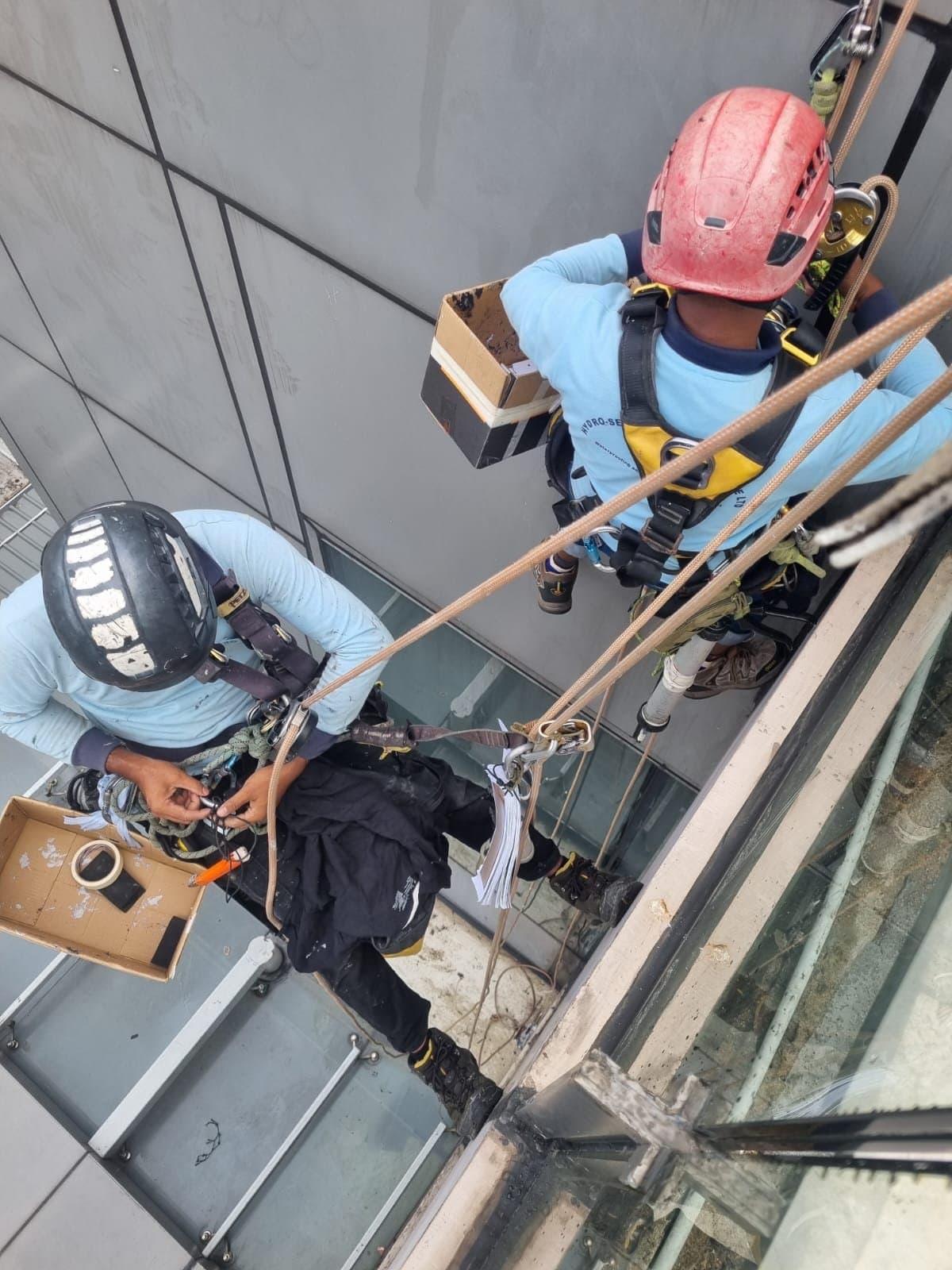 Hydroseal IRATA rope-access technicians in full PPE applying façade silicone sealant at height on a suburban retail mall in the Jurong Lake District, Singapore