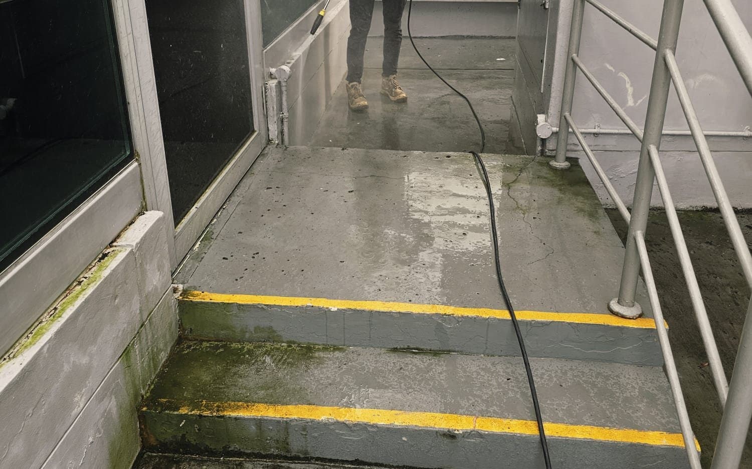 Hydroseal technician pressure washing green algae growth from an external wall base and concrete steps at a building in Singapore