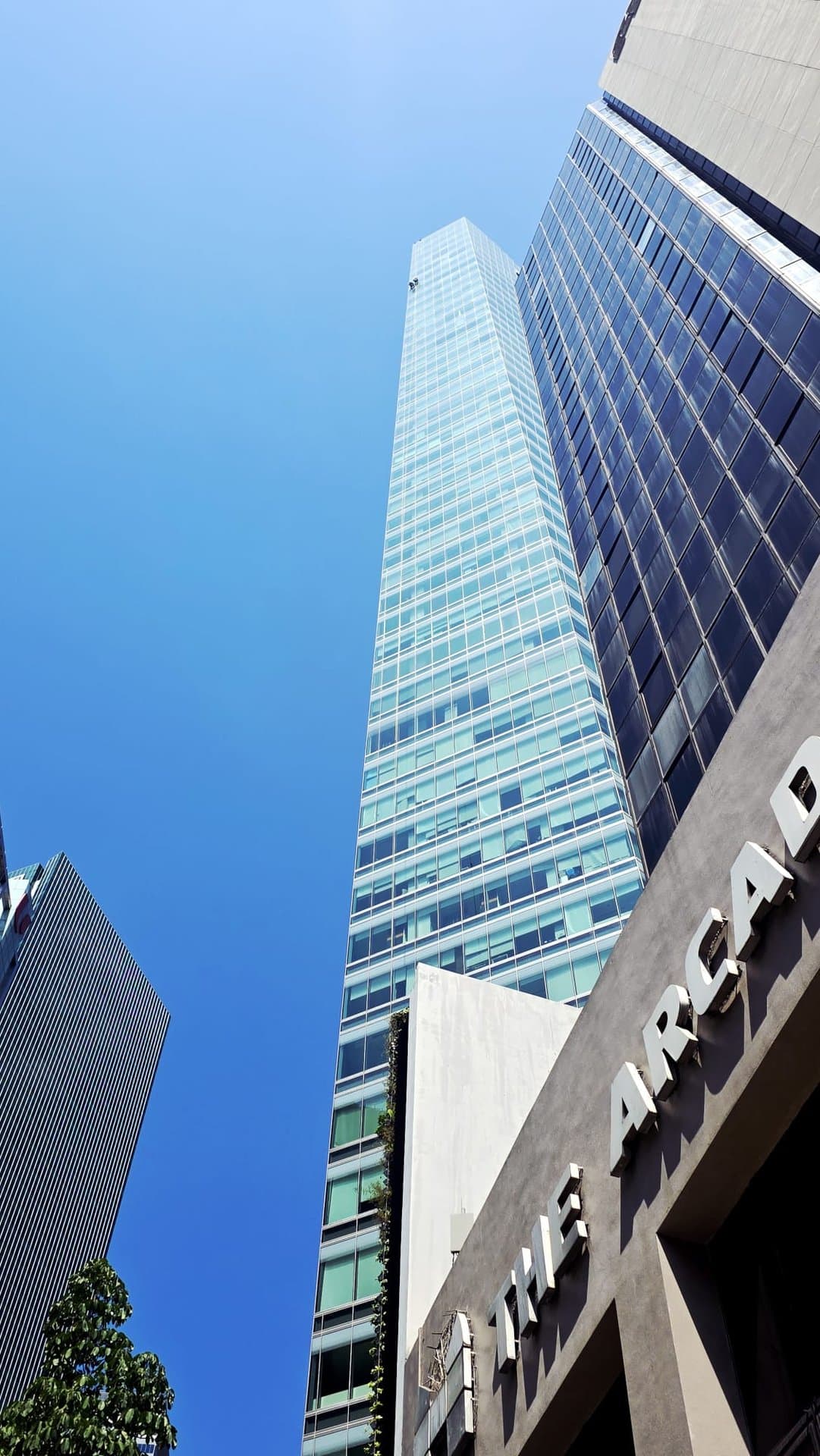 Hydroseal façade sealant and waterproofing works on a Grade-A glass office tower in Singapore’s Raffles Place financial district, viewed from street level into a clear blue sky
