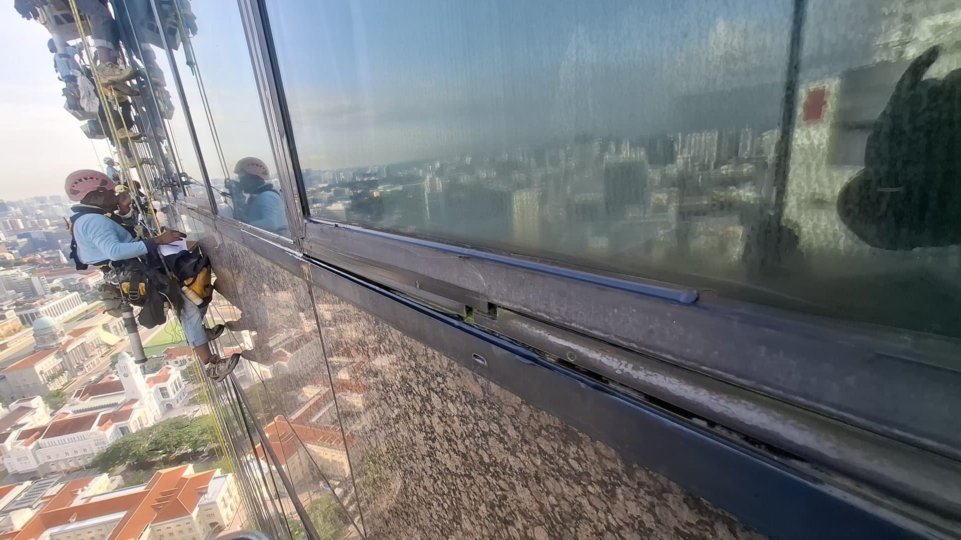 Hydroseal IRATA rope-access technicians renewing a sealant joint on a high-rise glass façade in Singapore's CBD to stop water leaking in
