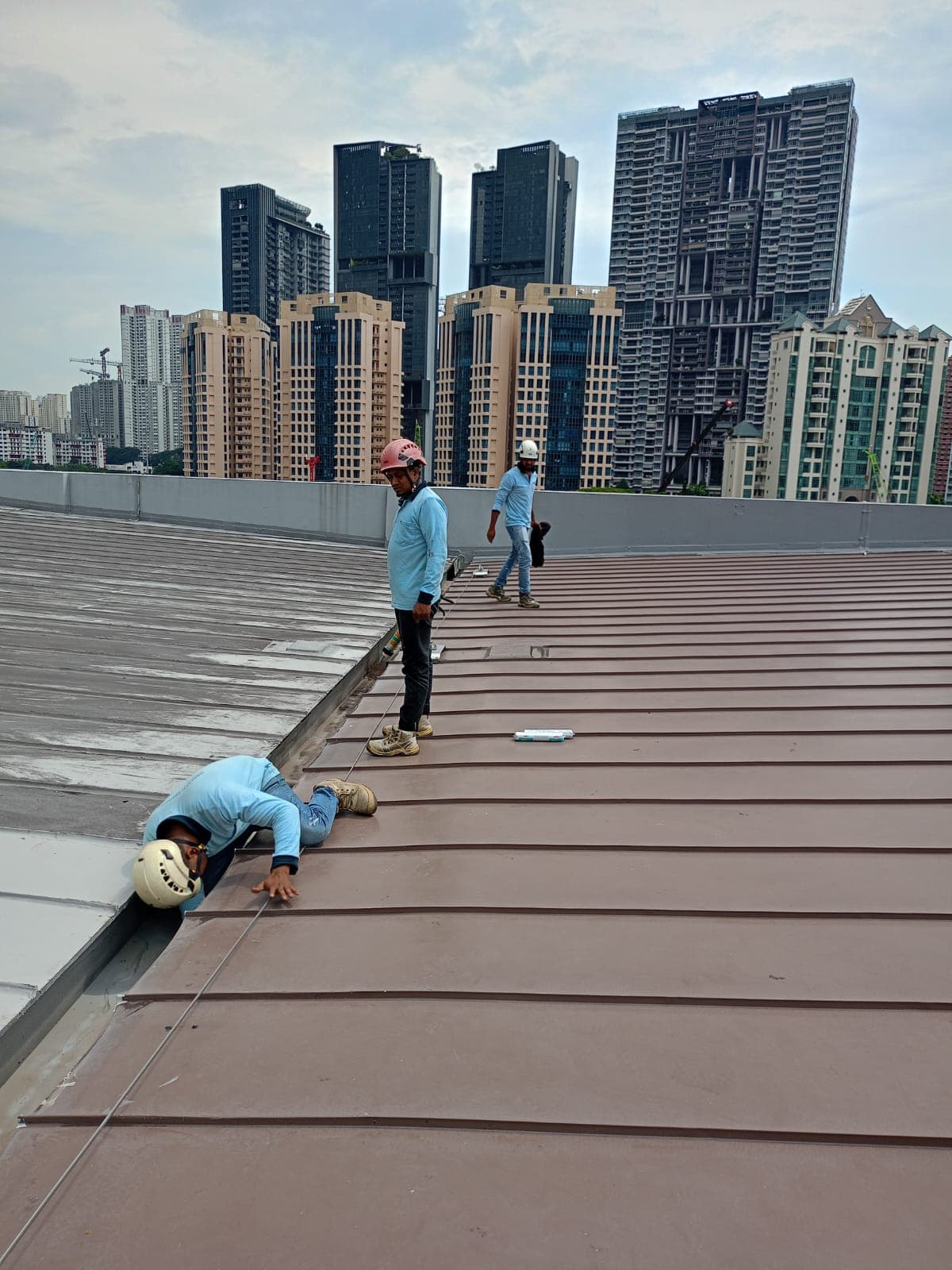 Hydroseal technicians waterproofing a large standing-seam metal roof with the Singapore skyline behind