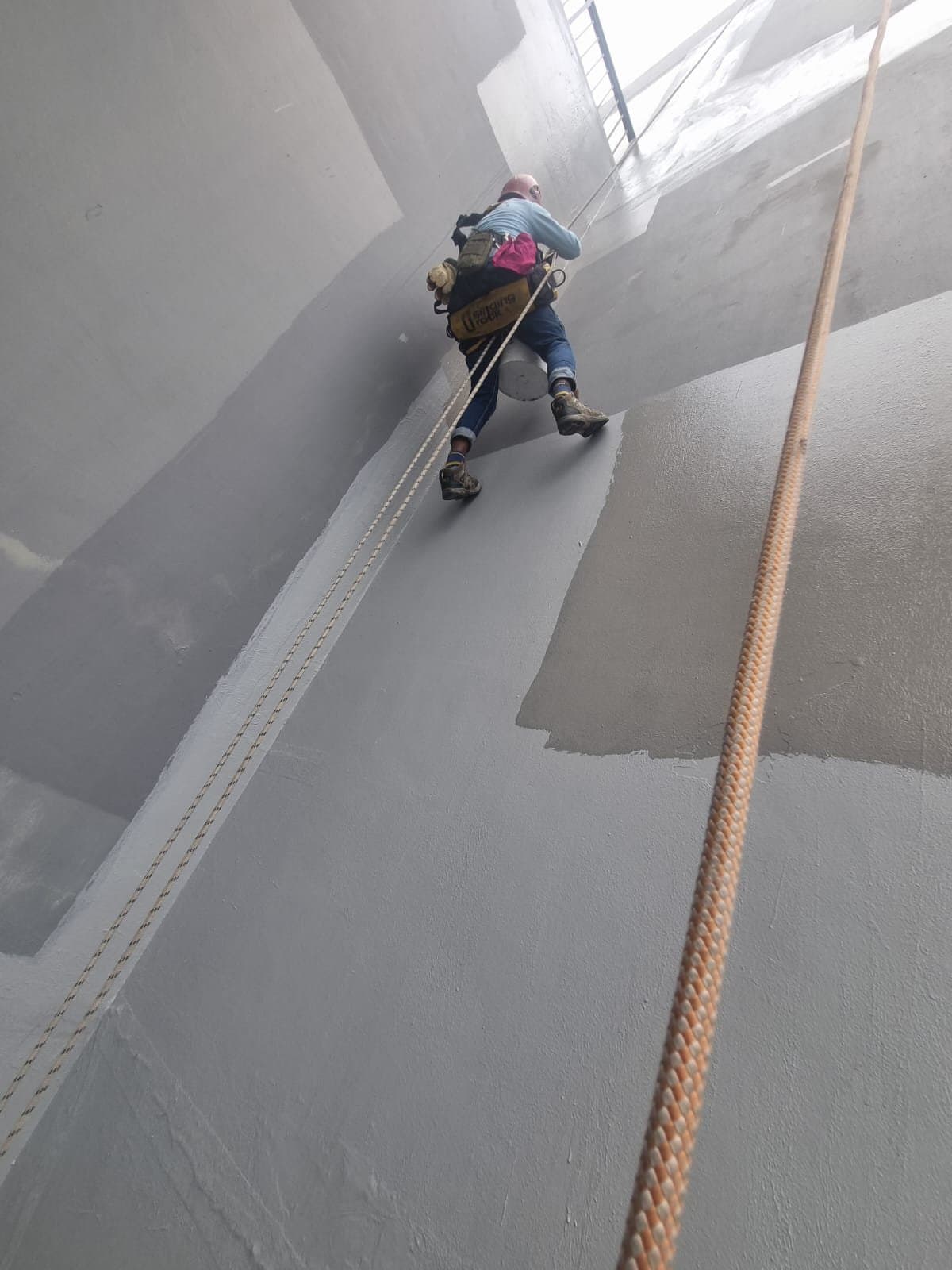 Hydroseal IRATA rope-access technician in full harness and PPE abseiling a granite façade to renew sealant joints on a multi-storey commercial building in Singapore