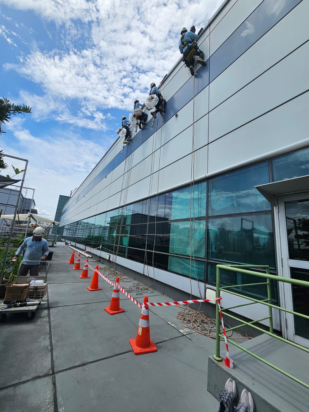 Hydroseal rope-access team working across a commercial building cladding façade under a blue Singapore sky