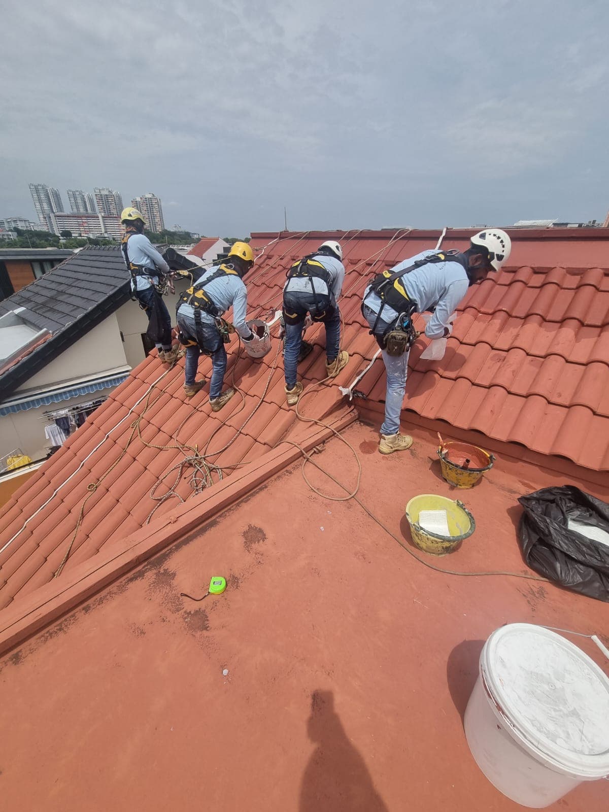 Four Hydroseal technicians waterproofing a red-tiled pitched roof on a Singapore landed home